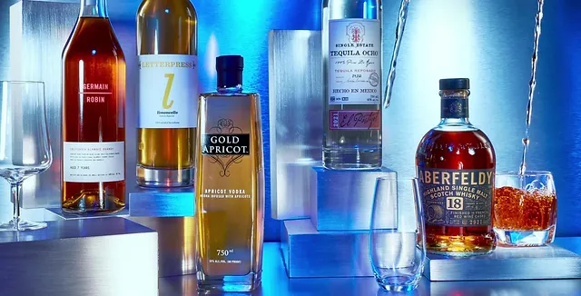 A selection of premium liquor bottles and glasses, illuminated with a modern blue background, featuring apricot vodka, single malt whiskey, and other high-quality spirits.