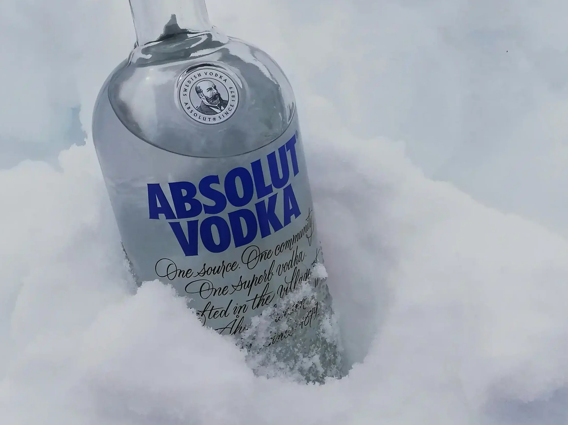 A bottle of Absolut Vodka placed in fresh snow, symbolizing its crisp and smooth qualities, ideal for winter gatherings.