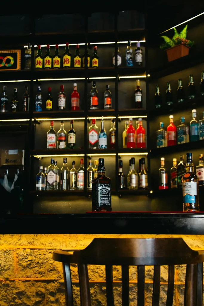 Modern bar with a wooden chair, illuminated liquor shelf featuring Jack Daniel's, The Glenlivet, and various spirits